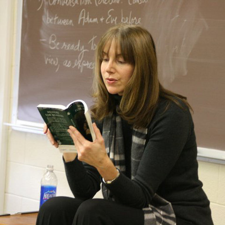 woman sitting in a classroom reading a book a loud.